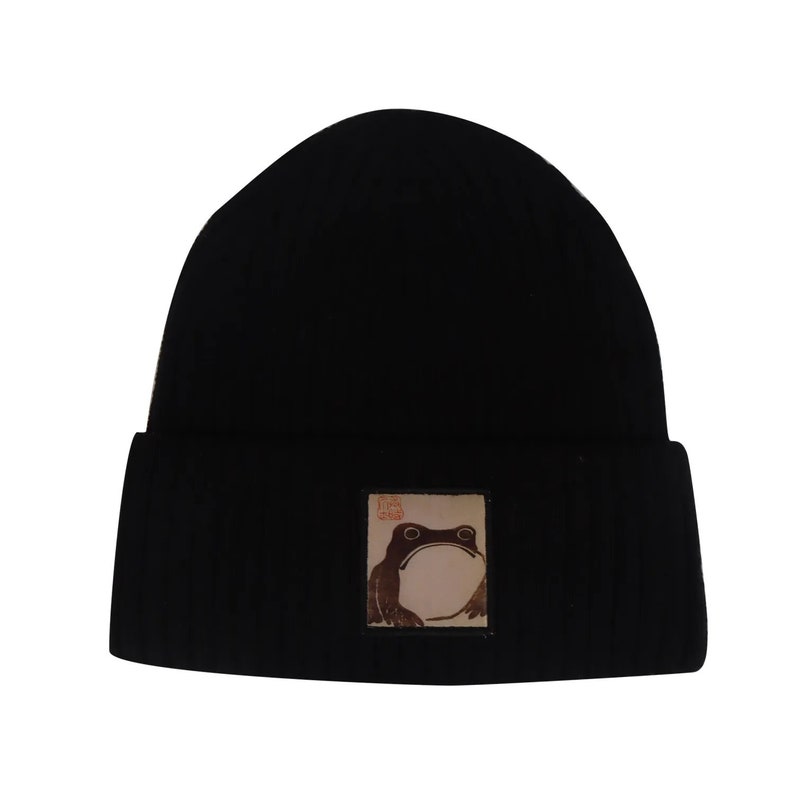May include: Black knit beanie with a brown frog graphic patch. The patch has the text "First Class" in red.
