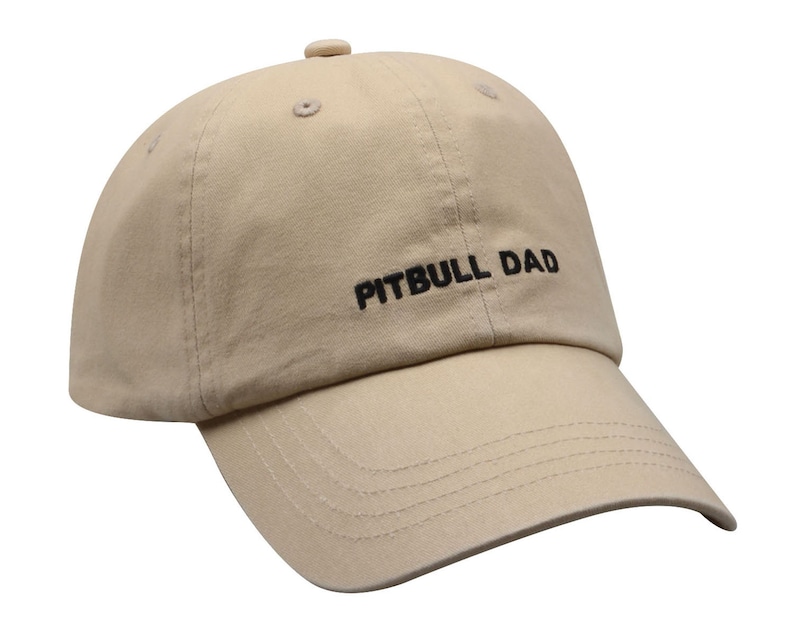 May include: A beige baseball cap with black embroidery that reads "PITBULL DAD".