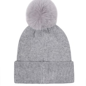 Pode incluir: Um gorro cinzento de malha com um grande e fofo pompom no topo. O chap&eacute;u tem uma textura canelada e uma aba dobrada. Este chap&eacute;u de inverno &eacute; um acess&oacute;rio elegante para o frio.