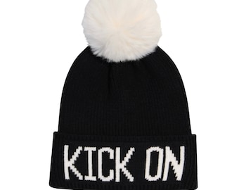 Puede incluir: Gorro de punto negro con un pompón blanco y las palabras "Kick On" en letras blancas.