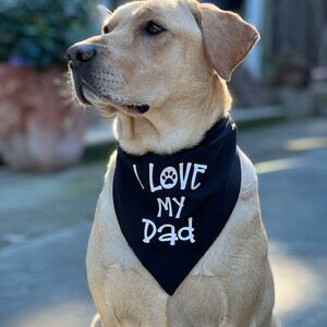 May include: A light brown dog wearing a black bandana with white text that says "I LOVE MY Dad" with a paw print symbol.