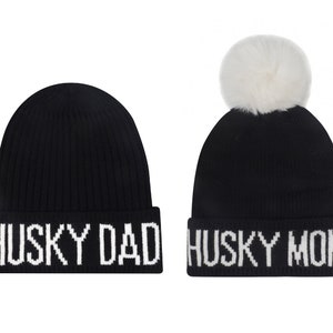 May include: Two black knit beanies with white pom poms and white text. One beanie says "Husky Dad" and the other says "Husky Mom".