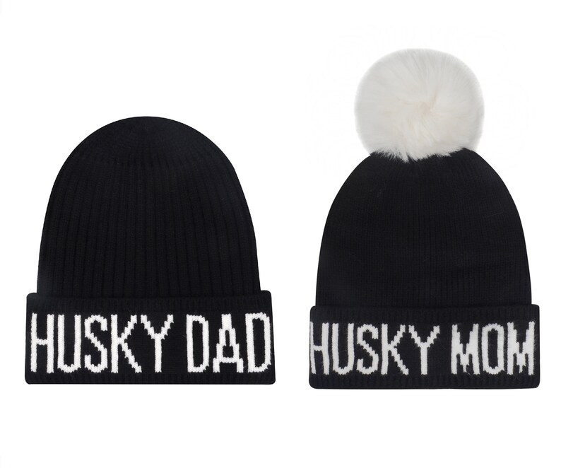 May include: Two black knit beanies with white pom poms and white text. One beanie says "Husky Dad" and the other says "Husky Mom".