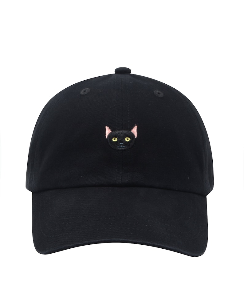K&ouml;nnte beinhalten: Eine schwarze Baseballkappe mit einem gestickten schwarzen Katzenkopf mit rosa Ohren und gelben Augen.