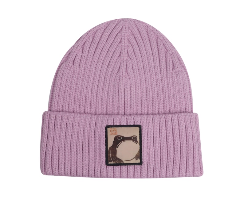 May include: A light purple knitted beanie with a brown frog patch. The patch has Japanese characters on it.