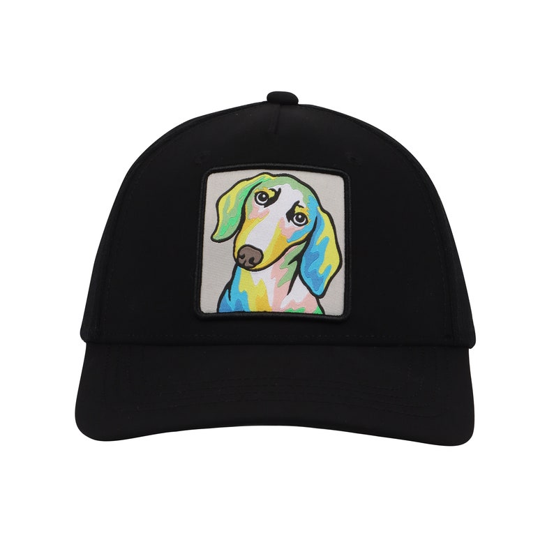 Op de afbeelding: Zwarte truckercap met een kleurrijk cartoon-dackel-patch op de voorkant.