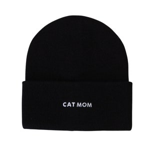 Puede incluir: Gorro de punto negro con el texto "CAT MOM" bordado en blanco.