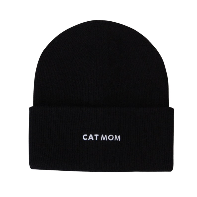 Puede incluir: Gorro de punto negro con el texto "CAT MOM" bordado en blanco.