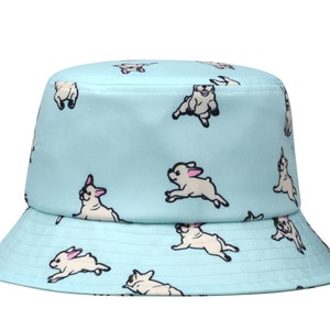 May include: A light blue bucket hat with a white French bulldog pattern. The hat has a wide brim and a flat crown.
