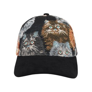 May include: A black baseball cap with a patterned design featuring multiple cat faces in shades of brown, gray, and orange. The cap has a black brim and a small black button on top. The cat faces have green eyes.