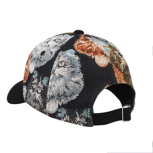 May include: A black baseball cap with a curved brim and adjustable strap. The cap features a woven design with images of cats in shades of gray, orange, and blue. The cap has a black button on top.
