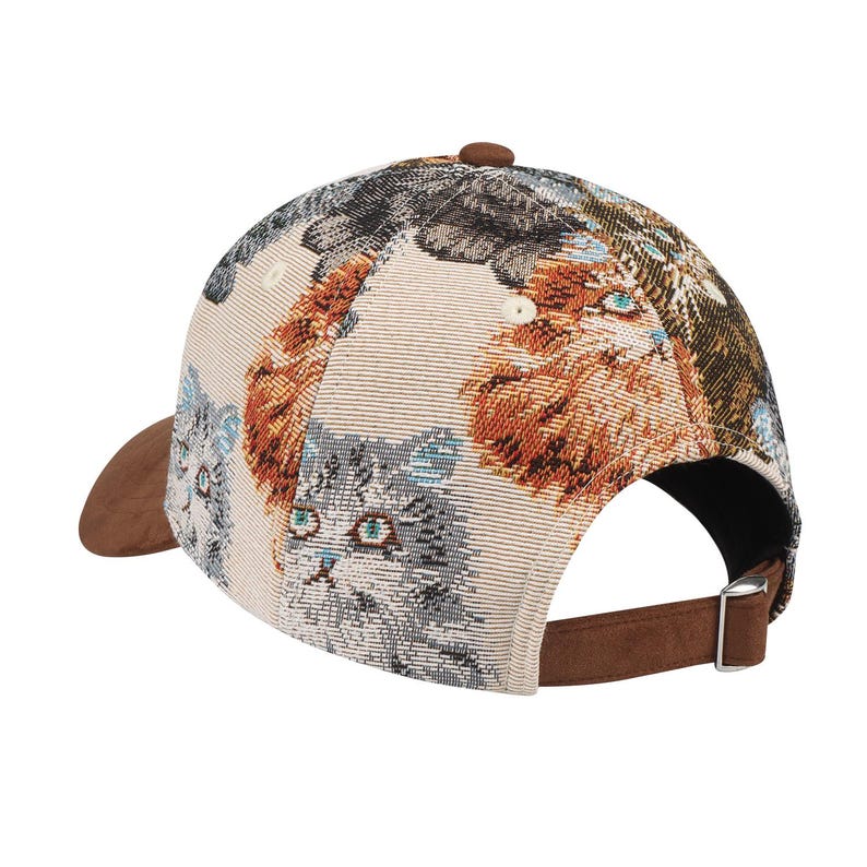 May include: A baseball cap featuring a tapestry-like design of various cat faces in shades of gray, orange, and brown. The cap has a brown suede brim and adjustable strap. The background is a beige color.