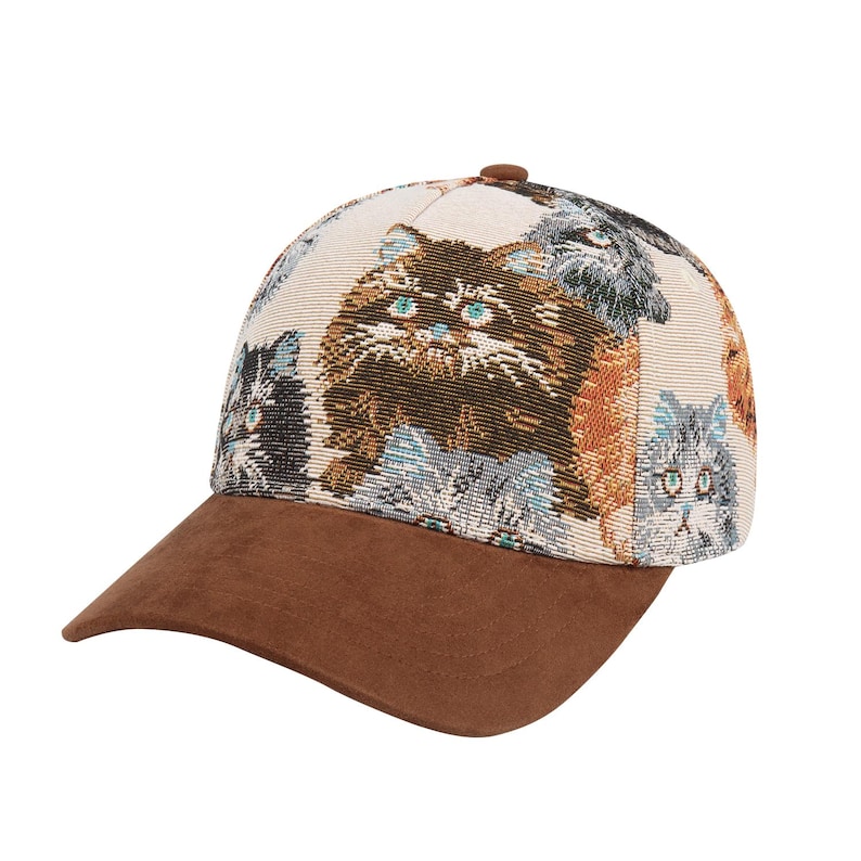 May include: A baseball cap with a brown suede brim and a cream-colored crown. The crown features a repeating pattern of various cat faces in shades of brown, gray, and blue. The cap has a brown button on top.