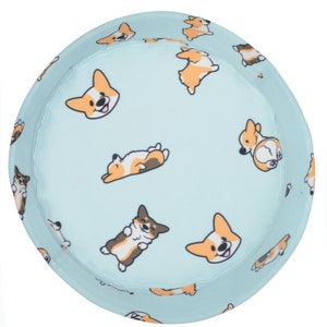 May include: A light blue bucket hat with a pattern of cartoon corgis in various poses. The corgis are brown, white, and orange.