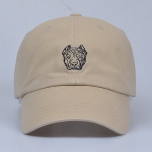 May include: A beige baseball cap with a black embroidered image of a pit bull's head.