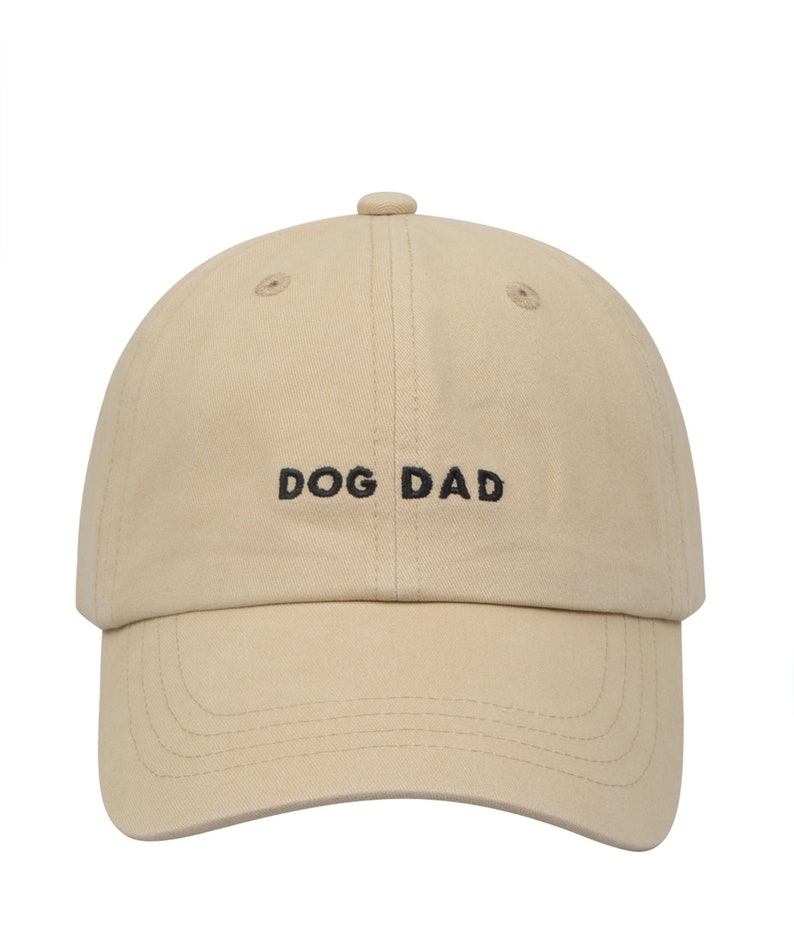 May include: A beige baseball cap with black embroidery that reads "DOG DAD".