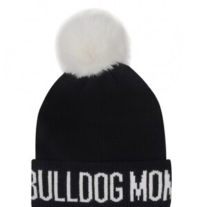 Pode incluir: Gorro de malha preto com um pompom branco no topo. O chap&eacute;u apresenta o texto "BULLDOG MON" em letras brancas na aba dobrada. Um acess&oacute;rio de inverno.