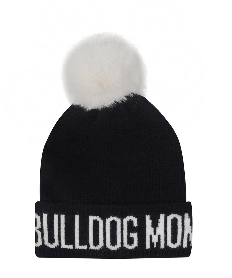 Pode incluir: Gorro de malha preto com um pompom branco no topo. O chap&eacute;u apresenta o texto "BULLDOG MON" em letras brancas na aba dobrada. Um acess&oacute;rio de inverno.