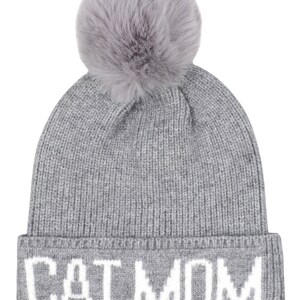 Puede incluir: Gorro de punto gris con un pomp&oacute;n esponjoso en la parte superior y las palabras "CAT MOM" en letras blancas en el pu&ntilde;o.