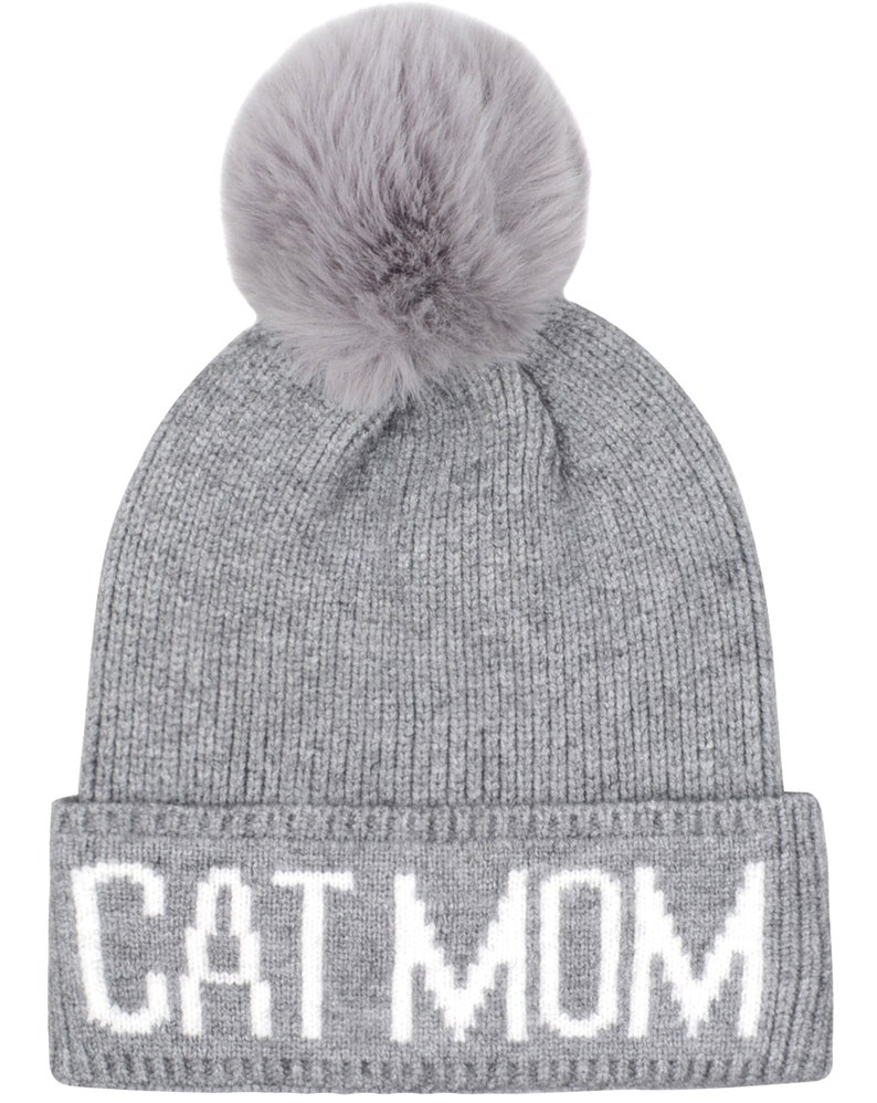 Puede incluir: Gorro de punto gris con un pomp&oacute;n esponjoso en la parte superior y las palabras "CAT MOM" en letras blancas en el pu&ntilde;o.