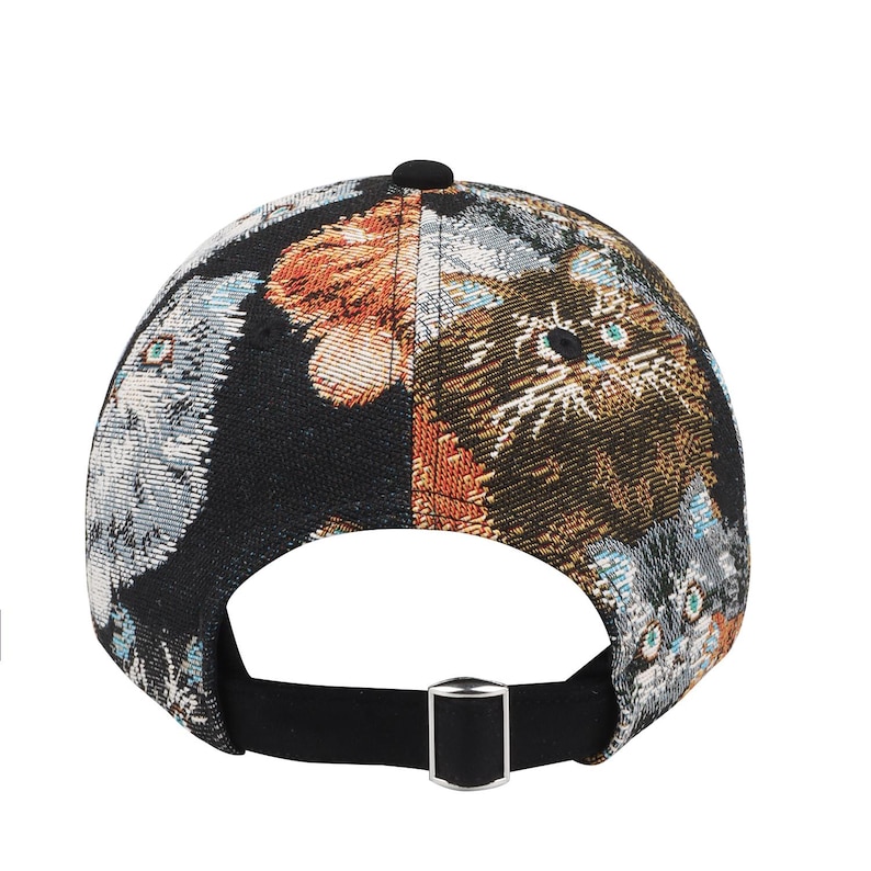 May include: A black baseball cap with a tapestry-like design featuring cat faces in shades of brown, orange, gray, and blue. The cap has a black brim and a silver-colored adjustable buckle.