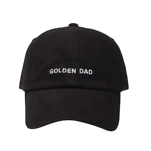 May include: Black baseball cap with white embroidered text that reads "GOLDEN DAD".