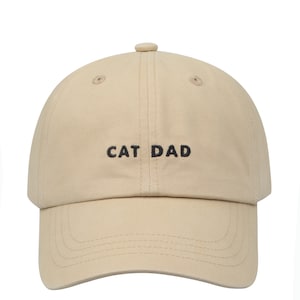 May include: A beige baseball cap with black embroidery that reads "CAT DAD".