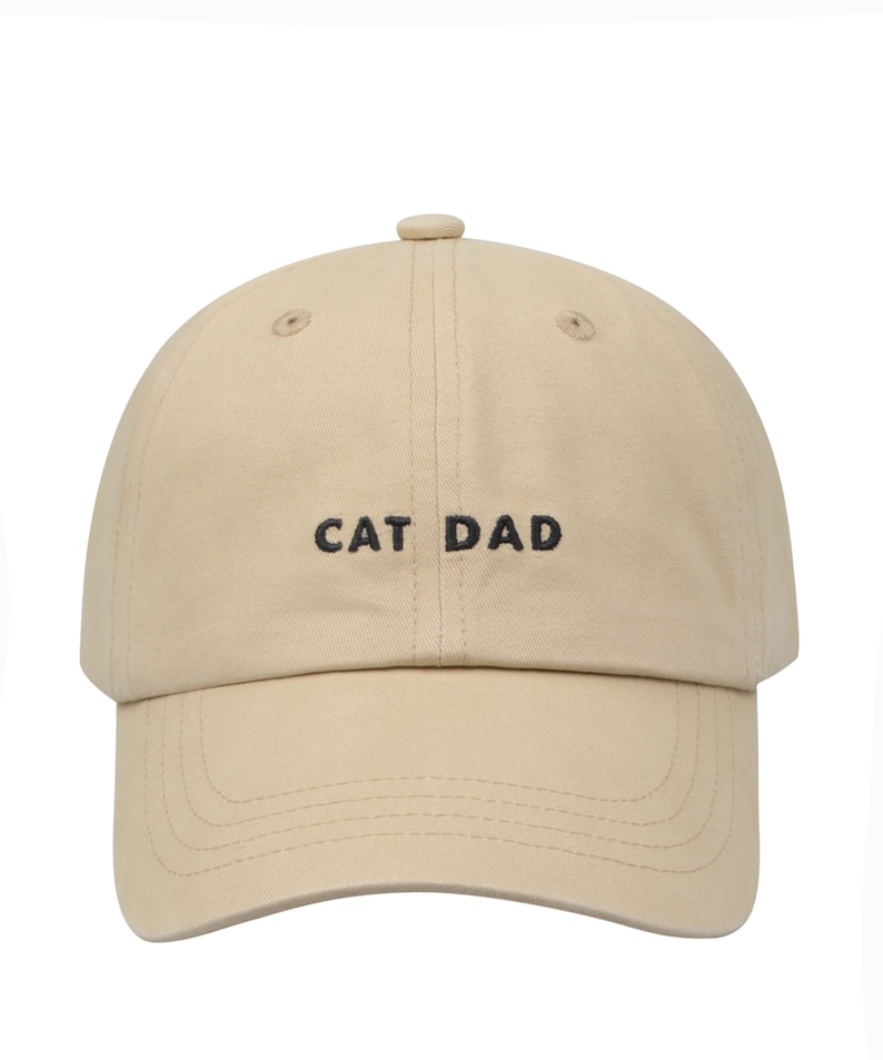 May include: A beige baseball cap with black embroidery that reads "CAT DAD".
