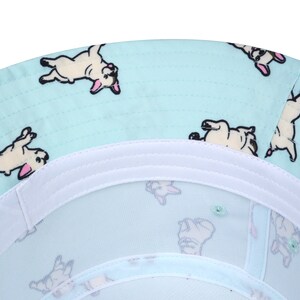 May include: A light blue bucket hat with a white band and a pattern of white French bulldogs on a light blue background.