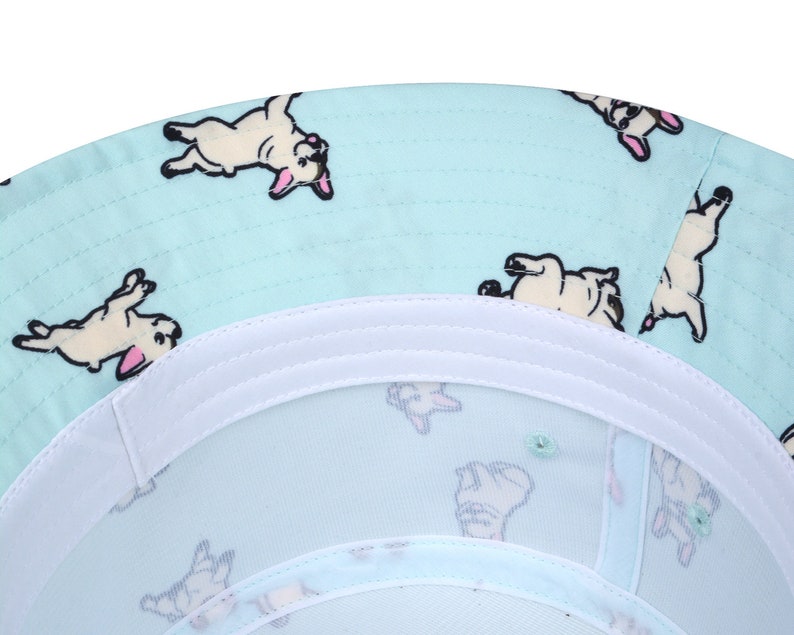 May include: A light blue bucket hat with a white band and a pattern of white French bulldogs on a light blue background.