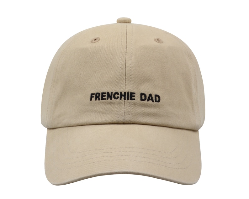 May include: A beige baseball cap with black embroidered text that reads "FRENCHIE DAD".