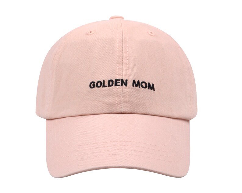 May include: A pink baseball cap with the text "GOLDEN MOM" embroidered in black.