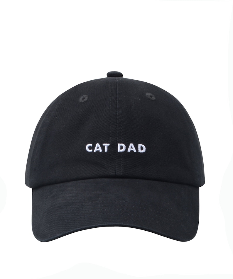 May include: A black baseball cap with white embroidered text that reads "CAT DAD".