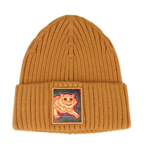 May include: A mustard yellow ribbed knit beanie featuring a square patch on the front cuff. The patch displays a colorful, stylized illustration of a cat with orange fur against a swirling, multi-colored background of blue, red, and green hues.