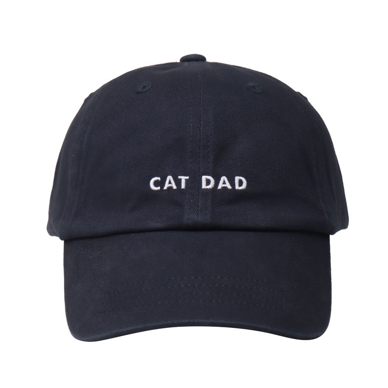 May include: A navy blue baseball cap with white embroidered text that reads "CAT DAD".