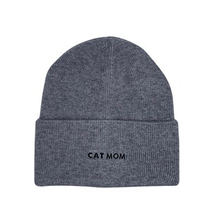 Puede incluir: Gorro de punto gris con el texto "CAT MOM" bordado en negro.