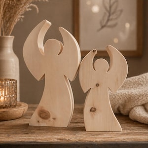 Könnte beinhalten: Zwei Holzengel-Figuren mit ausgebreiteten Flügeln. Die Engel sind aus hellem Holz gefertigt und haben ein schlichtes, minimalistisches Design. Sie stehen auf einer Holzoberfläche, im Hintergrund eine Vase und ein Kerzenhalter.