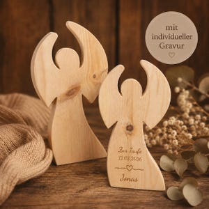Könnte beinhalten: Zwei helle Holzengel-Figuren mit glatten, geschwungenen Silhouetten. Der kleinere Engel ist mit dem Text Zur Taufe, 12.03.2026, einem Herzsymbol und dem Namen Jonas graviert. Die Holzmaserung ist auf beiden Figuren deutlich zu erkennen.