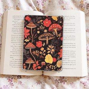 May include: A black tablet case with a vibrant autumn design. The case displays illustrations of mushrooms, flowers, and leaves in red, orange, yellow, and brown. The case is open on a book.