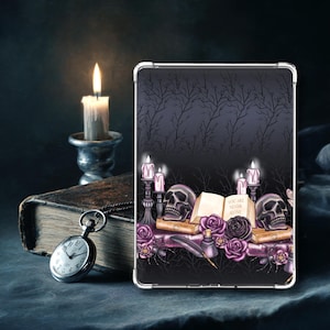 May include: A tablet case with a gothic design featuring skulls, candles, and roses. The case has a dark background with a tree branch pattern. The text on the open book reads "YOU ARE NEVER ALONE". A lit candle and a pocket watch are also visible.