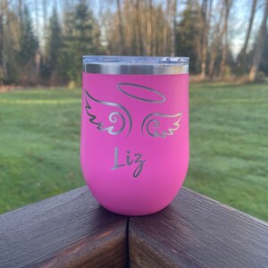 May include: Pink stainless steel tumbler with a silver angel wing design and the name "Liz" engraved on the front.
