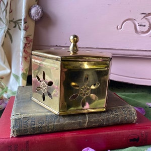 May include: A hexagonal brass box with a decorative floral pattern and a small knob on the lid. The box is sitting on top of two books.