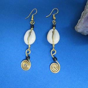 May include: A pair of gold earrings with white shell and black bead accents. The earrings feature a spiral design at the bottom.