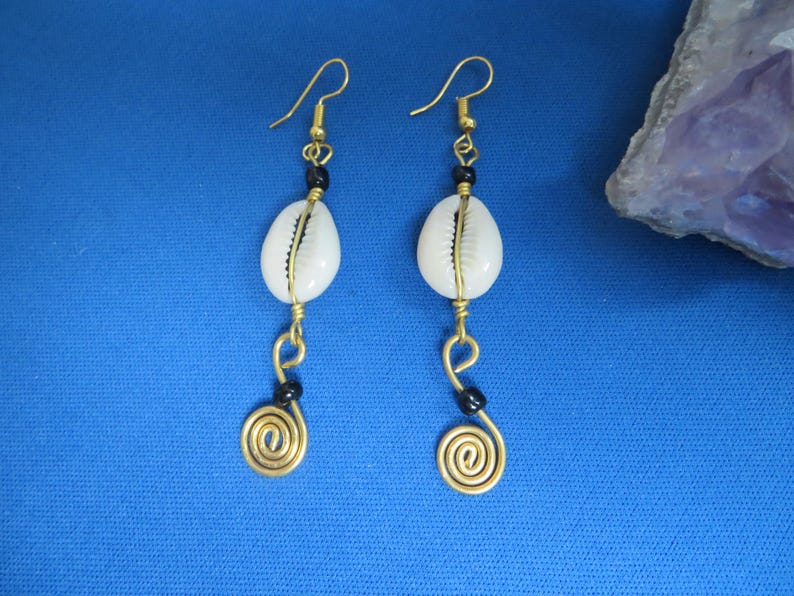 May include: A pair of gold earrings with white shell and black bead accents. The earrings feature a spiral design at the bottom.