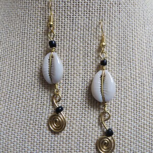 May include: Gold earrings with white cowrie shells and black beads. The earrings have a spiral design at the bottom.