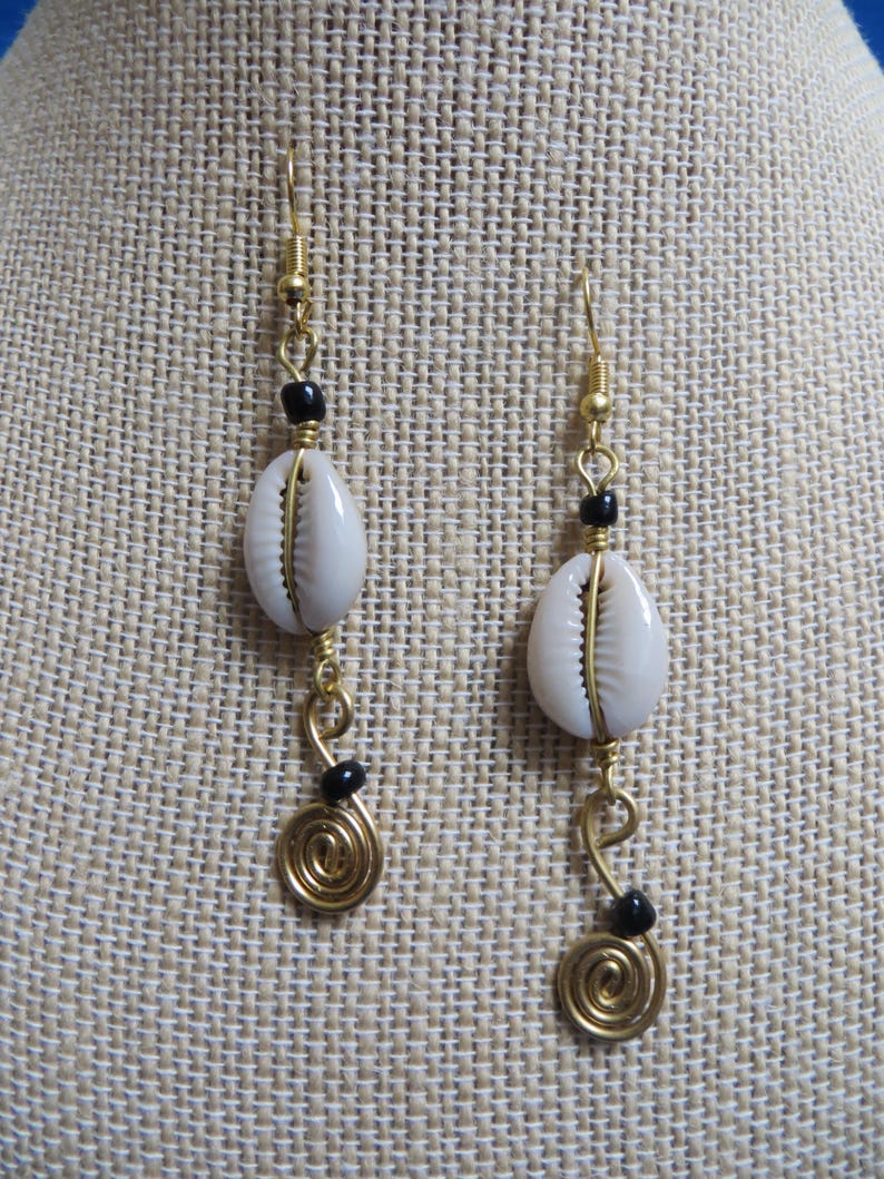 May include: Gold earrings with white cowrie shells and black beads. The earrings have a spiral design at the bottom.
