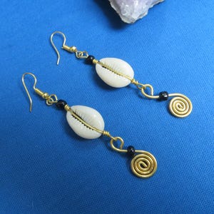 May include: A pair of gold earrings with white shell and black bead accents. Each earring features a spiral design at the bottom.