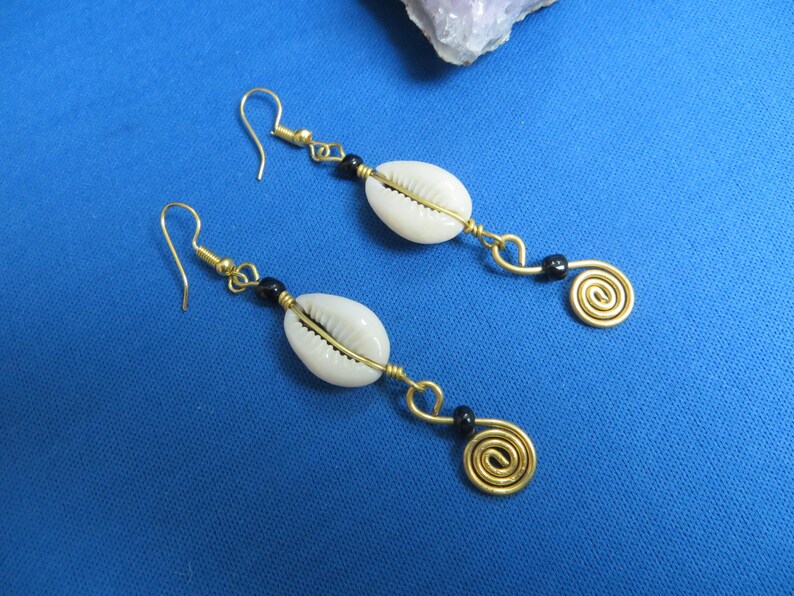 May include: A pair of gold earrings with white shell and black bead accents. Each earring features a spiral design at the bottom.