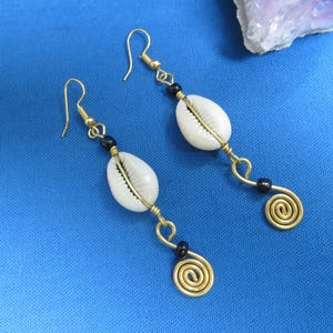 May include: A pair of gold earrings with white seashells and black beads. The earrings have a spiral design at the bottom.