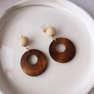 May include: A pair of wooden earrings with a brown circle design and a white wooden bead on each earring.